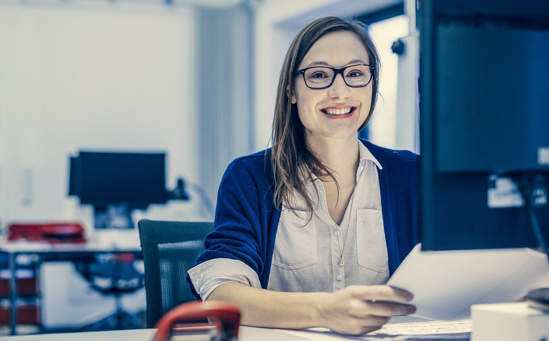 Mitarbeiterin im Öffentlichen Dienst sitzt lächelnd an ihrem Schreibtisch