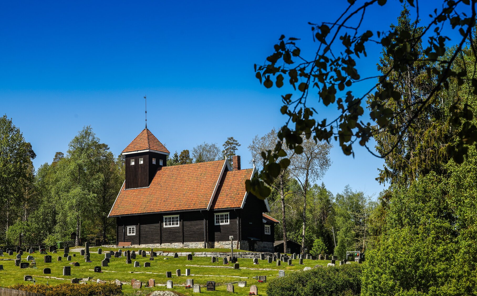 Bild von einem friedlichen Friedhof, wo eine Kirche und vereinzelte Gräber zu sehen sind.