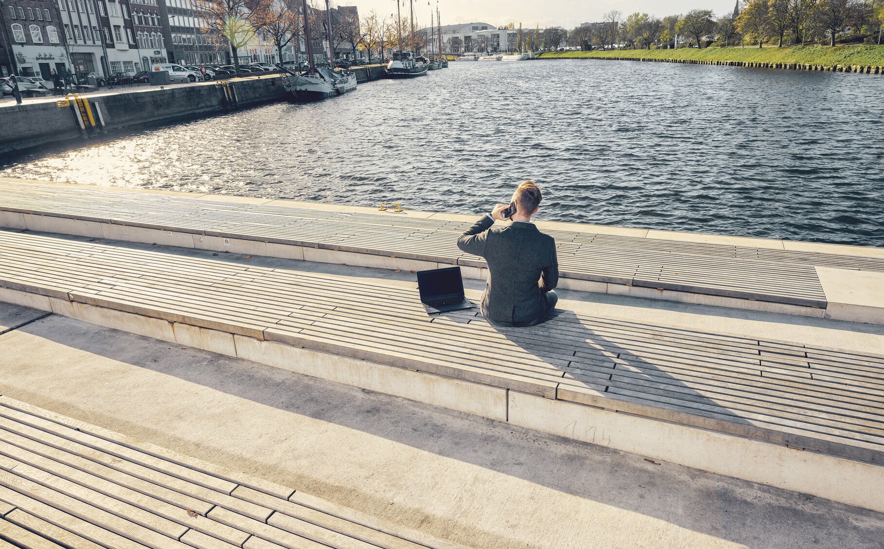 Ein telefonierender Mann sitzt auf einer Bank mit Ausblick auf Wasser.