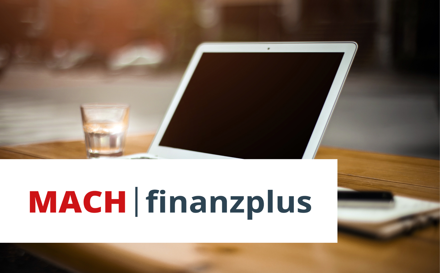 Ein Macbook, ein Glas Wasser, ein Notizblock und ein Handy liegen auf einem Tisch