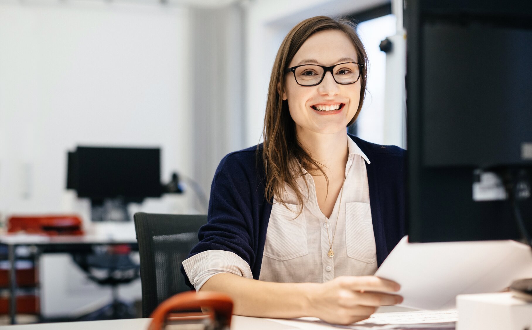 Eine lächelnde Frau sitzt im Büro und schaut in die Kamera.