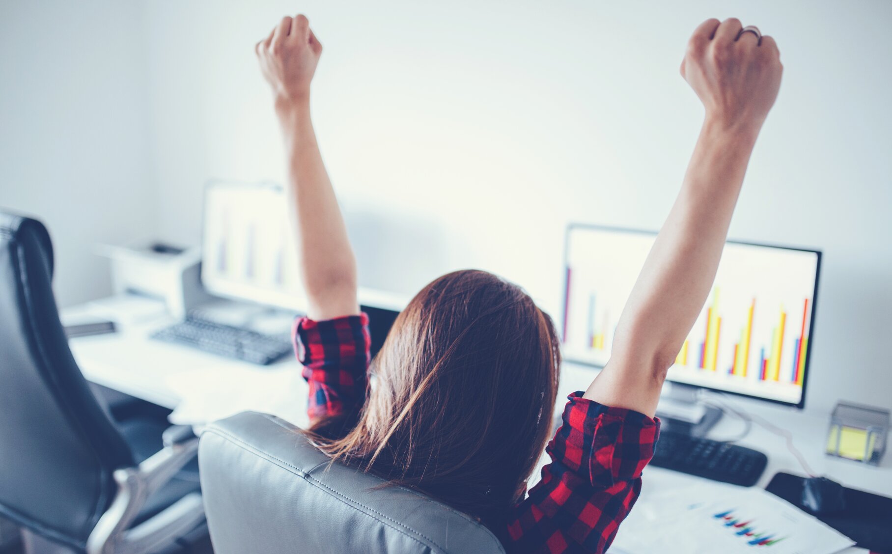 Frau sitzt am Schreibtisch und hebt beide Arme in die Luft.